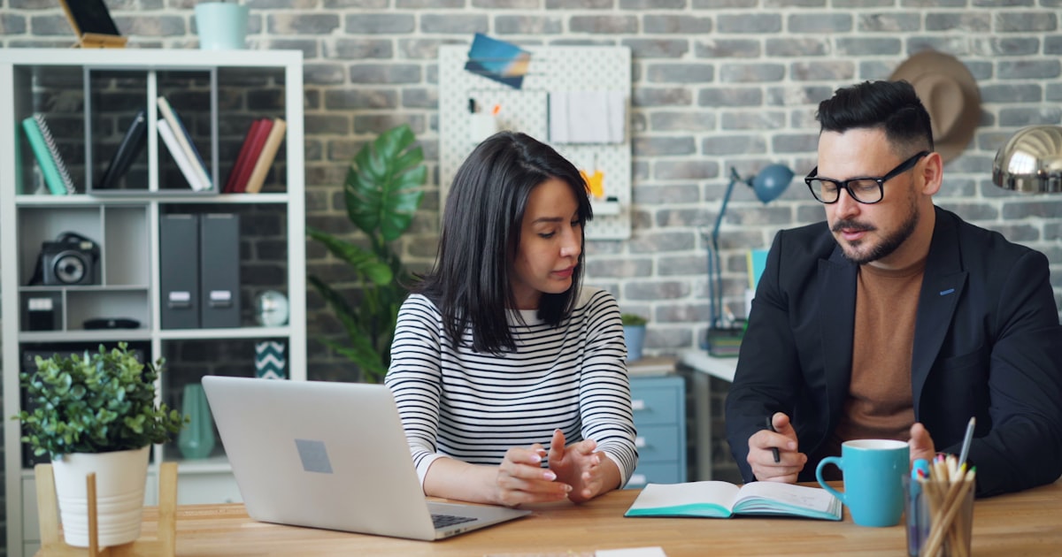 a man and a woman sitting at a table looking at a laptop