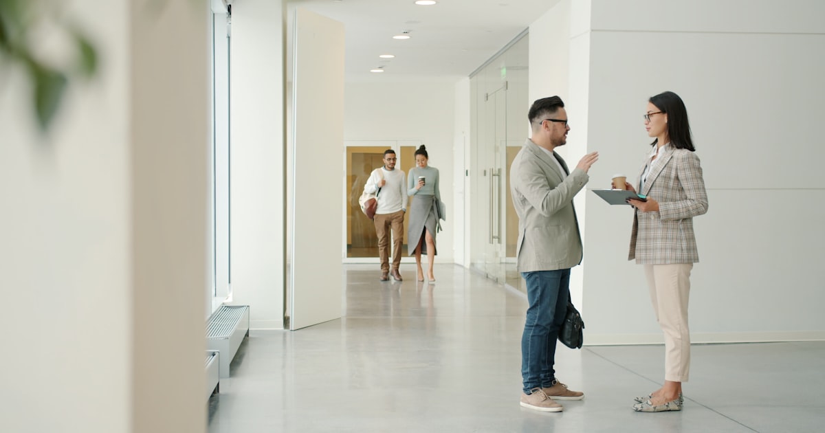 Two people talking in a modern office hallway.